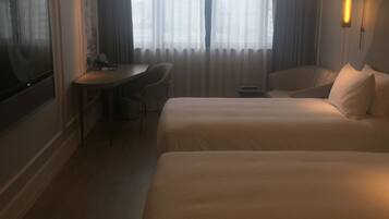 Habitación de hotel con dos camas, un escritorio, una silla, un televisor y una ventana con cortinas.