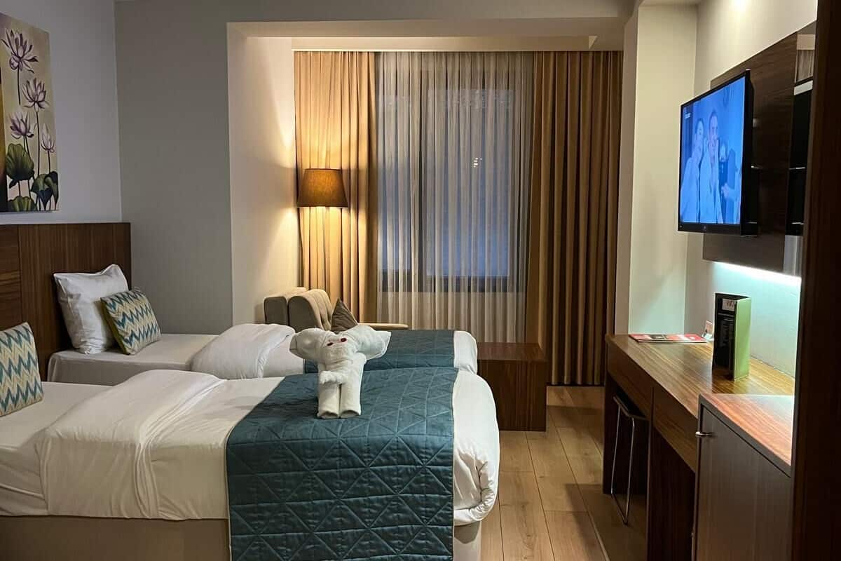 A hotel room with a bed, a desk, a television, and a window with curtains.