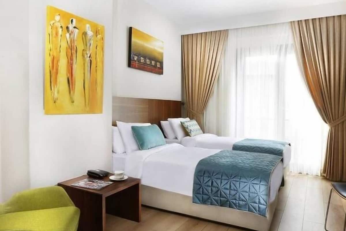 A hotel room with a large bed, a bedside table, a chair, and artwork on the walls.