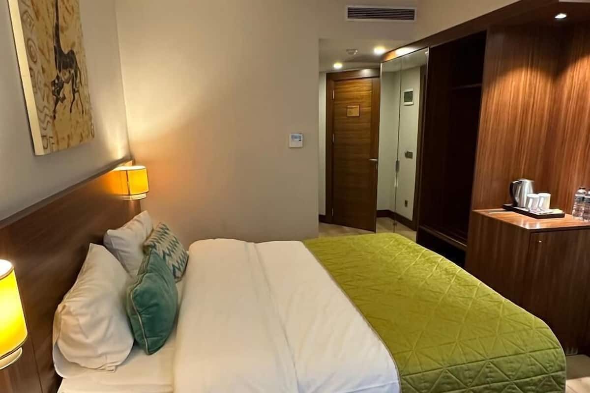 A hotel room with a bed, bedside table, and a green chair.