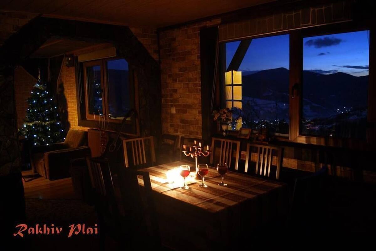 A cozy room with a wooden table, two chairs, a lit candle, and a Christmas tree.