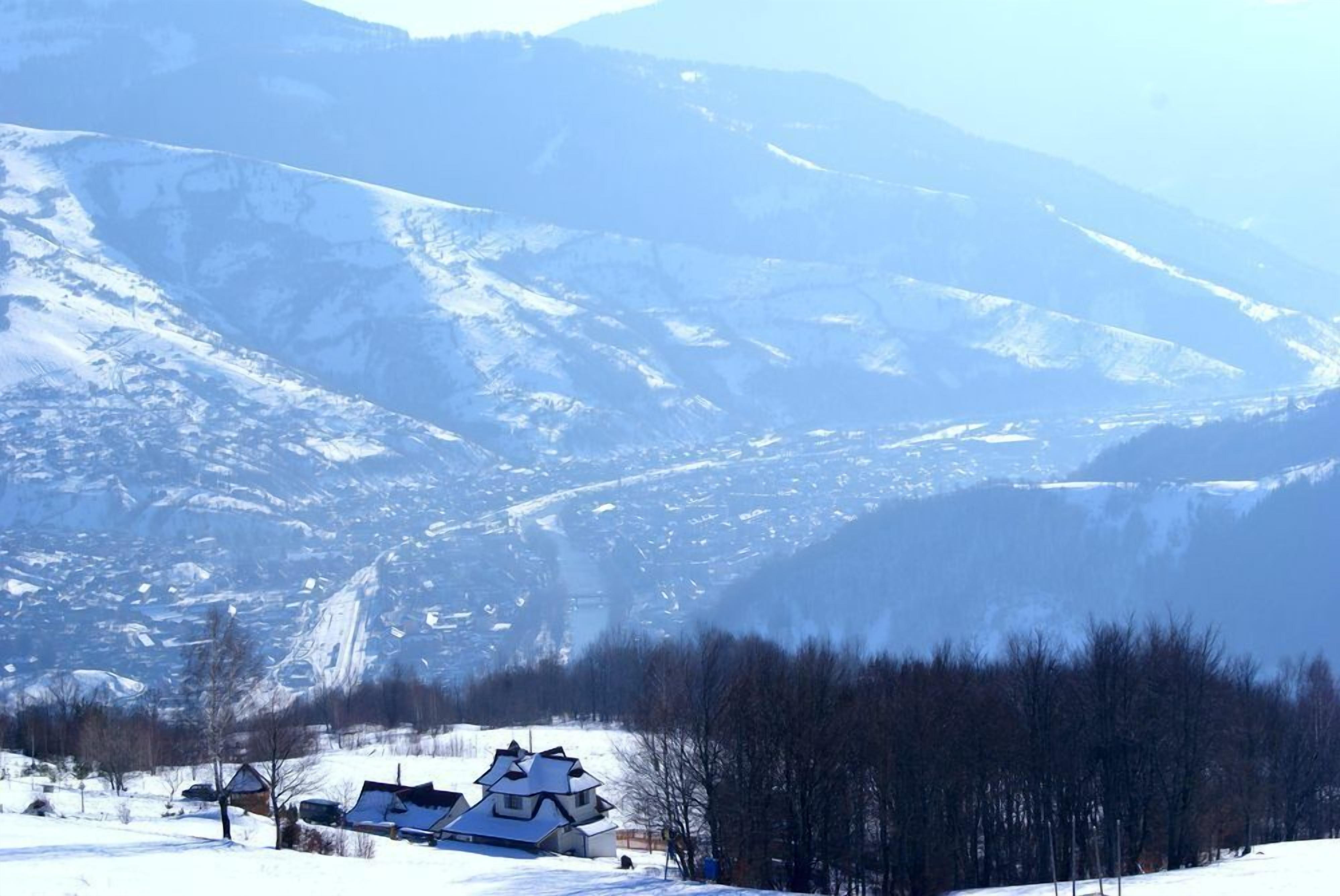 Un paysage montagneux enneigé, avec un bâtiment traditionnel doté d’un toit en pente et d’une petite annexe.