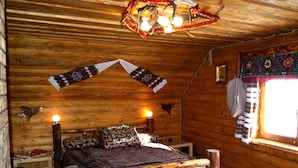 Een gezellig blokhutkamer met een houten bed, twee bedlampen, een gestreept deken en een decoratieve wandversiering.