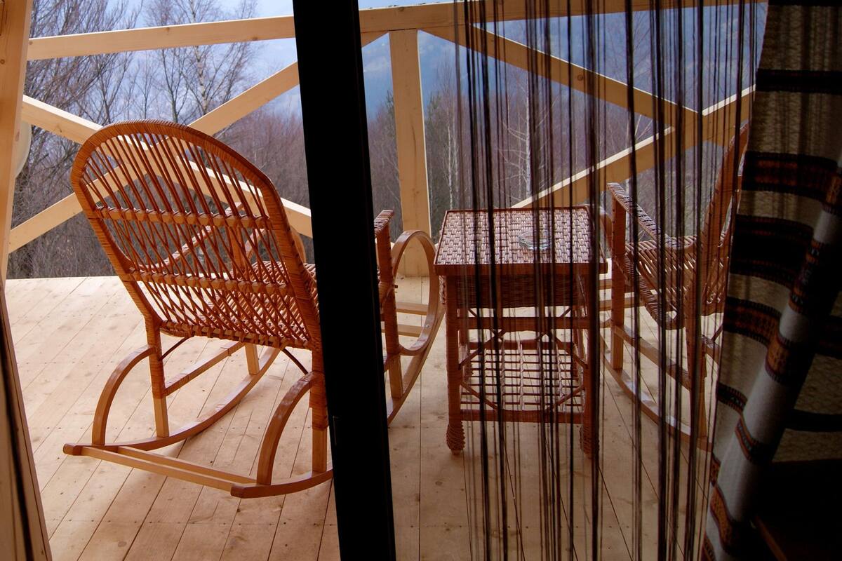 A wooden deck with a rocking chair and a small table, overlooking a mountainous landscape.