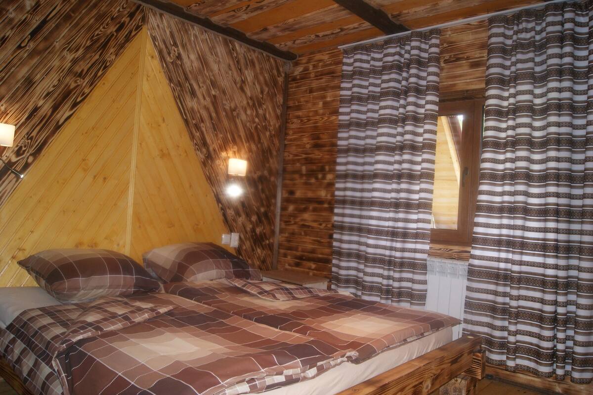 A cozy room with a wooden sloped ceiling, a bed with plaid bedding, and striped curtains.