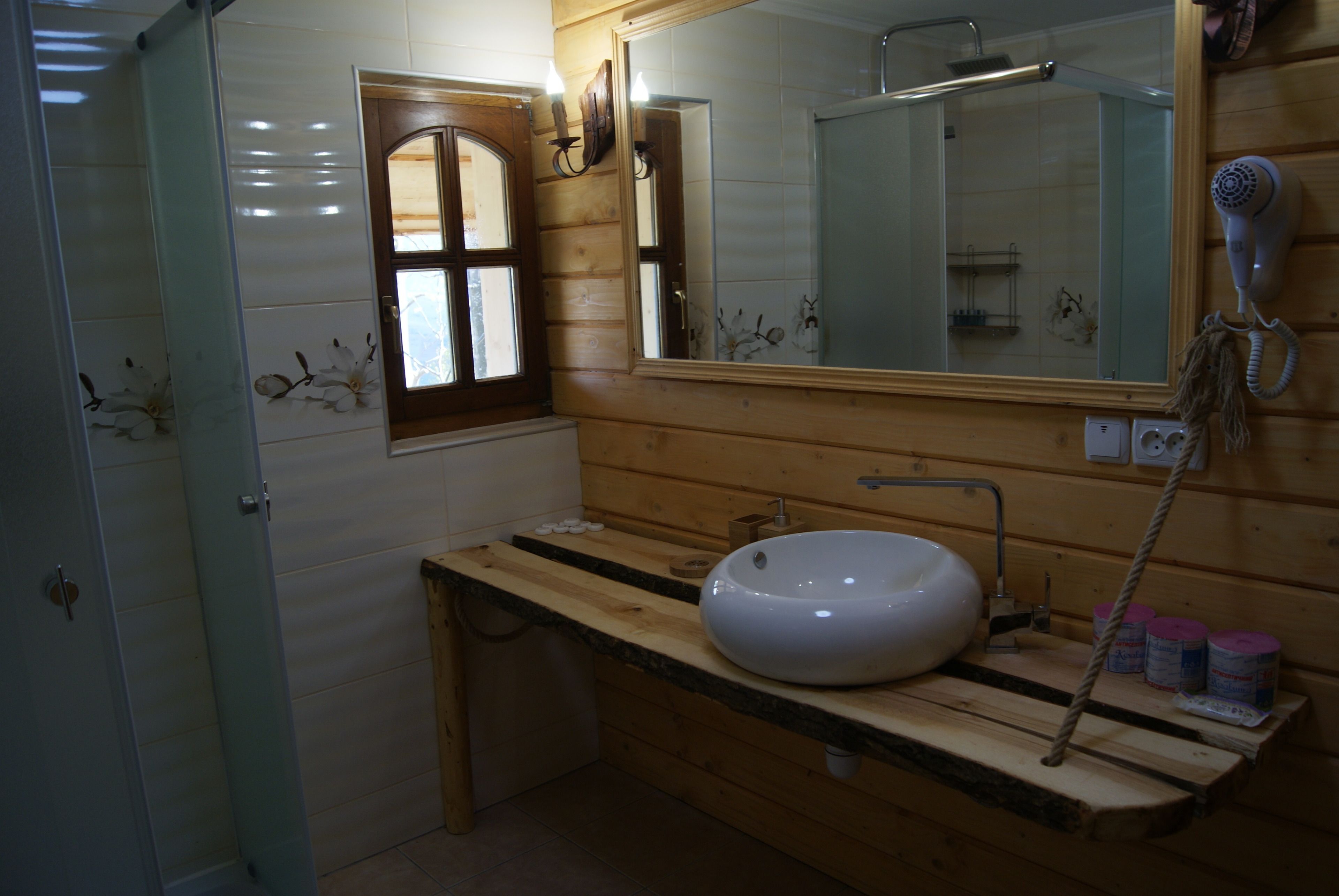 A bathroom with a wooden vanity, a large mirror, a white sink, and a hairdryer mounted on the wall.