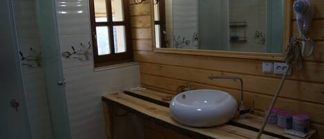 A bathroom with a wooden vanity, a large mirror, a white sink, and a hairdryer mounted on the wall.