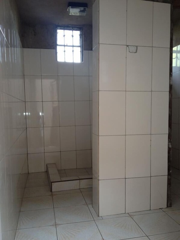 Un baño con piso de baldosas, una zona de ducha, una ventana pequeña y una puerta.