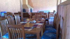 A dining area with wooden tables and chairs, a checkered table runner, and a blue cushioned bench. - Lake Chahafi  Resort (Kisoro)