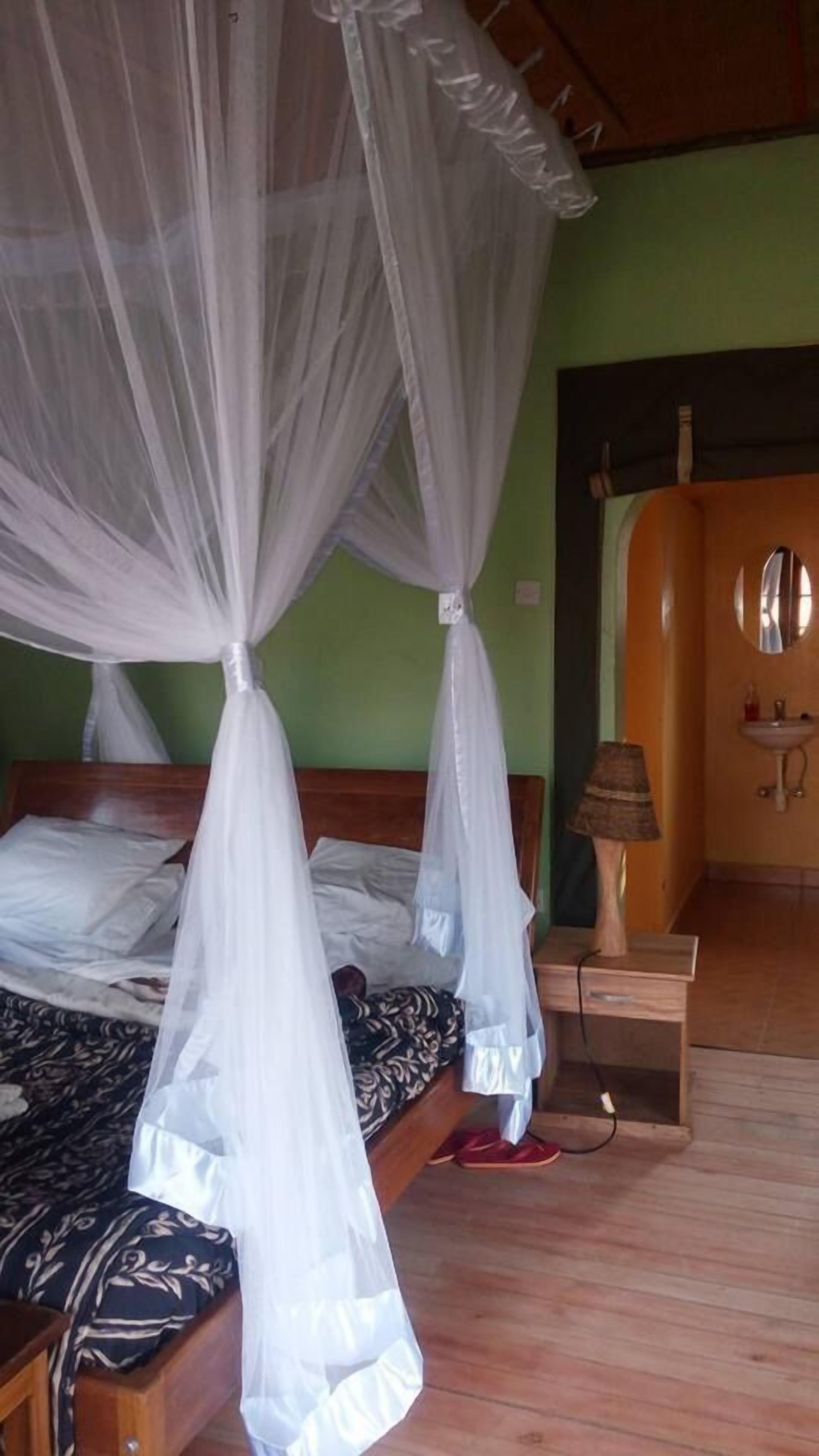 A room with a bed under a white canopy, a bedside table with a lamp, and a wooden wardrobe.