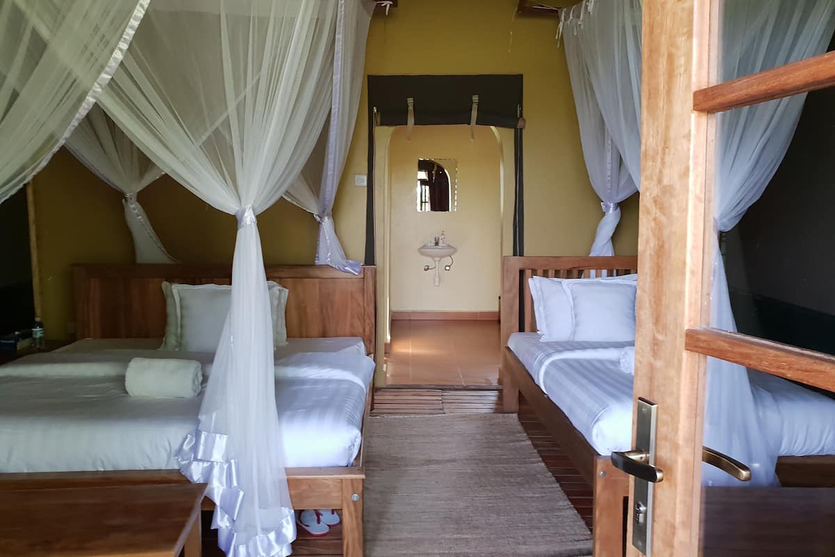 A room with two beds, each with a canopy, a small sink, and a mirror.