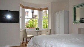 Un dormitorio con cama, televisión montada en la pared, ventana con vista a la vegetación y un armario blanco.