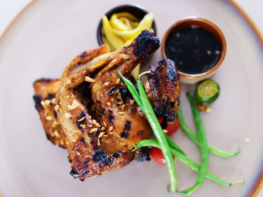 Un plato con pollo a la parrilla, una rodaja de lima, chile verde y un recipiente pequeño con salsa.