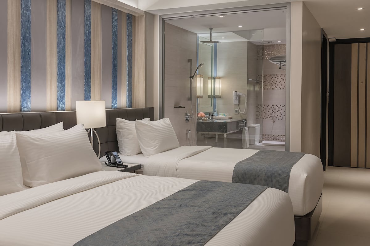 Habitación de hotel con dos camas, baño con ducha y un ventanal con cortinas a rayas.