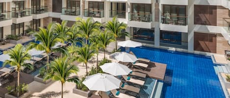 Un hotel moderno con piscina en la azotea, varios balcones y palmeras.