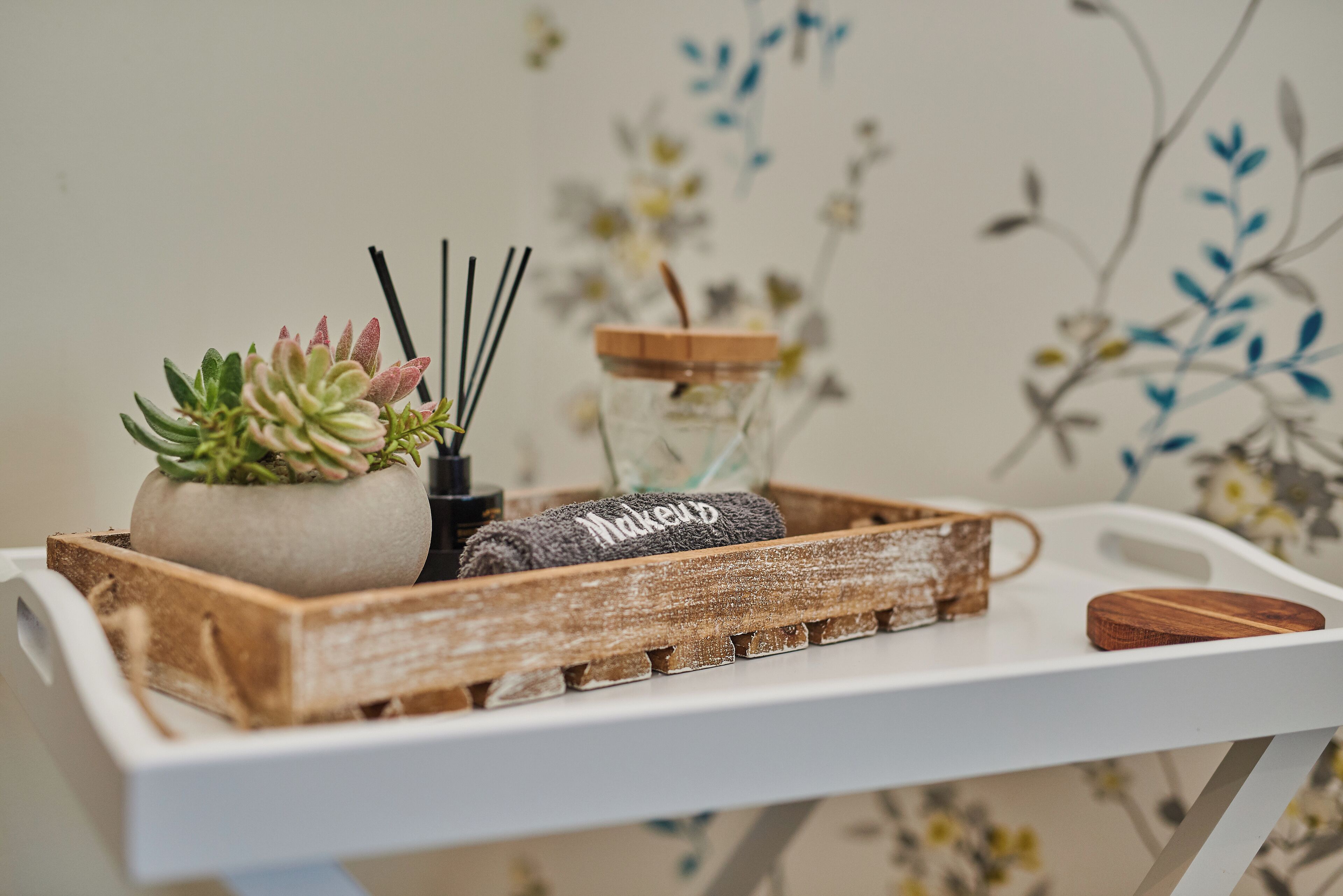 A wooden tray with a succulent plant, a rolled towel, and a glass jar with a straw.