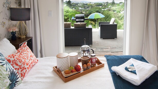 Ein Hotelzimmer mit einem Bett, einem Frühstücksbrett, Blick ins Freie und einer Terrasse mit Grill und Sitzgelegenheit.