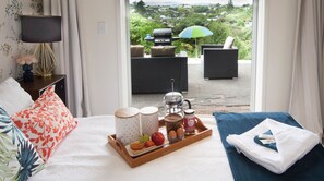 A hotel room with a bed, a tray with breakfast items, a view of the outdoors, and a patio area with a grill and seating. - The Queenslander Raglan (Raglan)