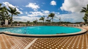 A swimming pool with a tiled deck, surrounded by palm trees and a clear sky. - 2/2 condo, with fantastic views of the beach (Marco Island)