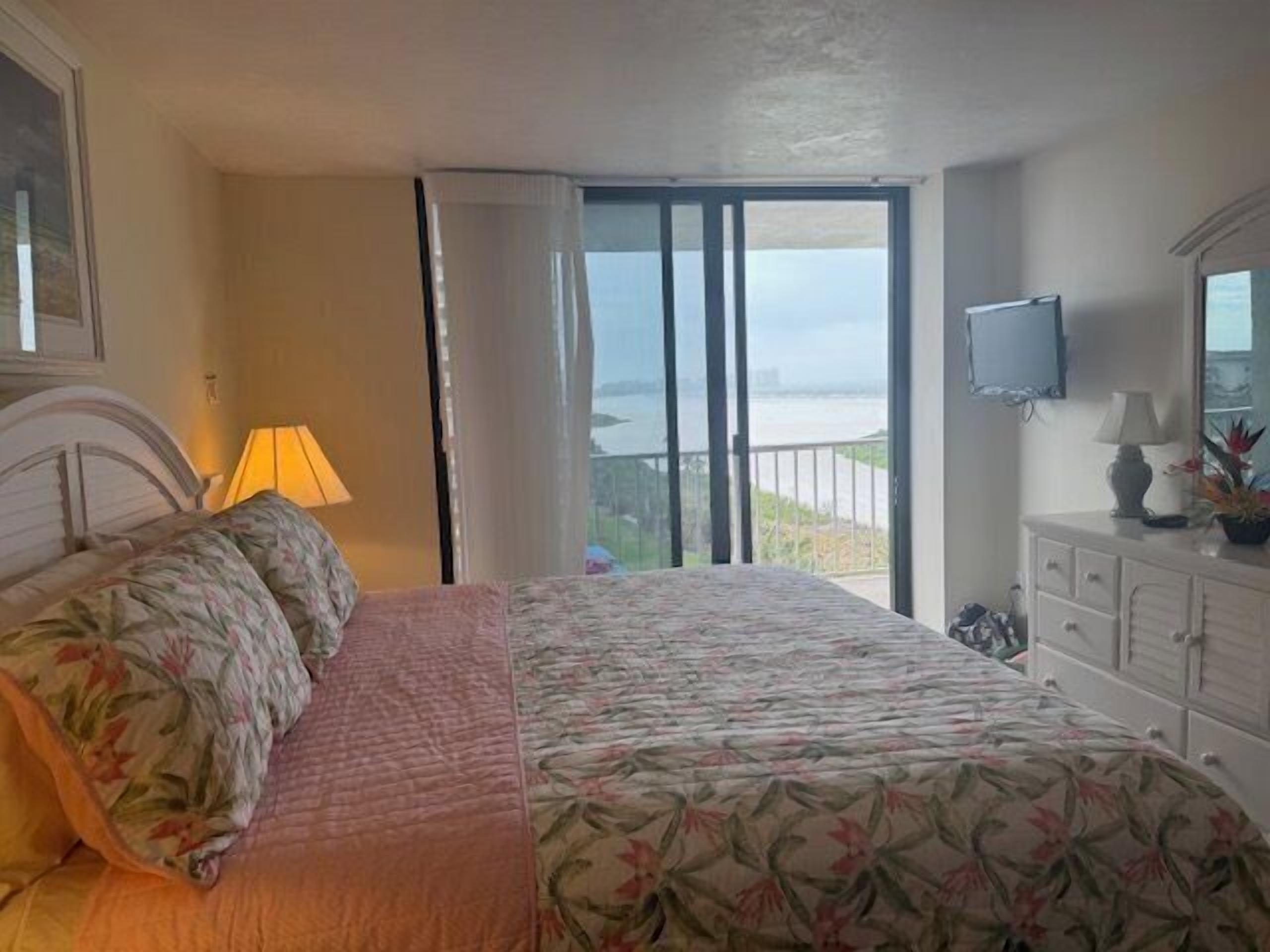 A hotel room with a bed, a TV, a balcony with a view, and a dresser with a mirror.