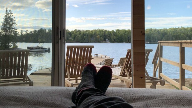 Una habitación con un amplio ventanal con vistas a un lago, sillones de madera en terraza y vista al agua.