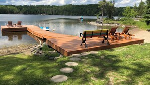 Muellé de madera que se adentra en un lago, con un banco y sillas en la plataforma.