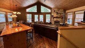 A spacious kitchen with a large island, wooden ceiling, stone fireplace, and large windows offering views of the outdoors. - Beautiful 5 Star Guest Cabin in the Mountains, steps from Lake Cle Elum (Ronald)