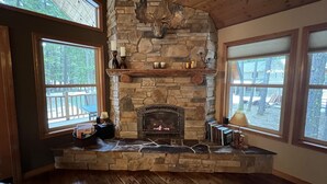 A stone fireplace with a mounted deer head, surrounded by windows offering views of the outdoors. - Beautiful 5 Star Guest Cabin in the Mountains, steps from Lake Cle Elum (Ronald)
