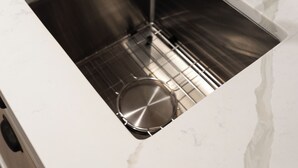 A stainless steel kitchen sink with a modern faucet, a white countertop, and a tiled backsplash.