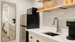 A modern kitchen with a refrigerator, microwave, coffee maker, and wooden shelves.
