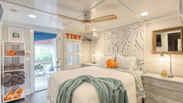 A bedroom with a bed, a ceiling fan, a nightstand, a dresser, a wardrobe, and a door labeled 'TINY'.