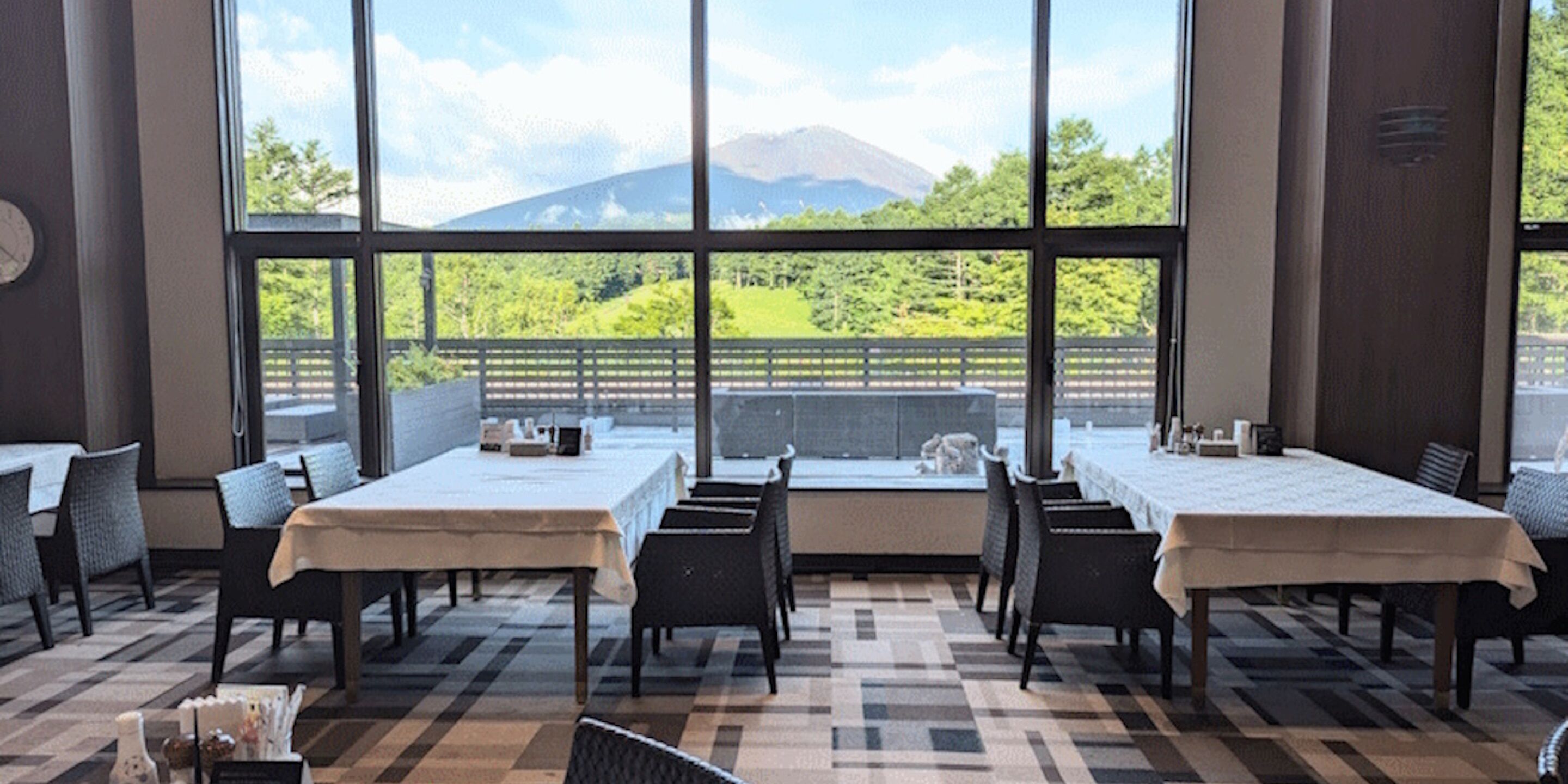 A dining area with tables and chairs, large windows with a view of a mountain and greenery.