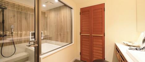 A bathroom with a glass shower enclosure, a wooden door, and a white sink.