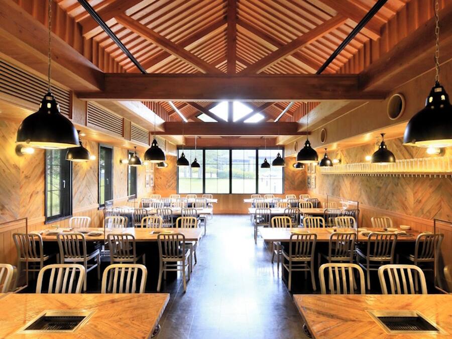 A spacious restaurant with high ceilings and wooden beams, featuring multiple tables and chairs arranged for dining.