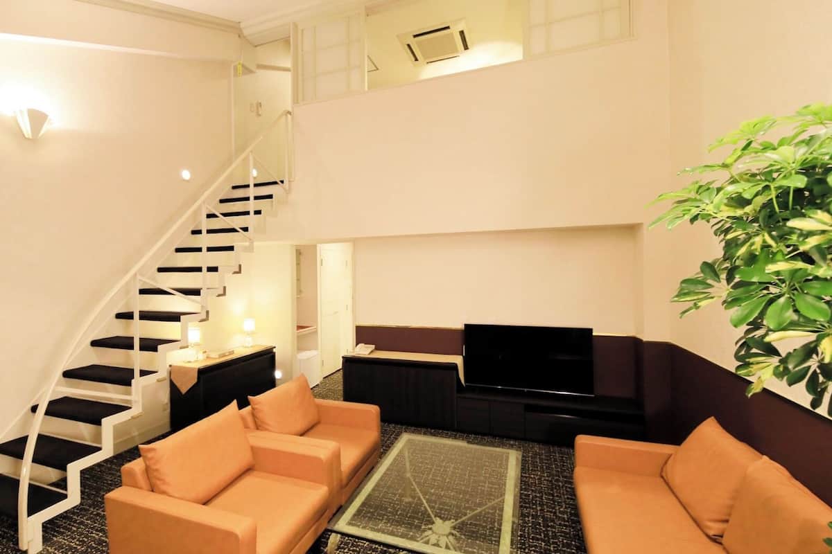 A modern living room with a staircase, a flat-screen TV, two sofas, and a coffee table.
