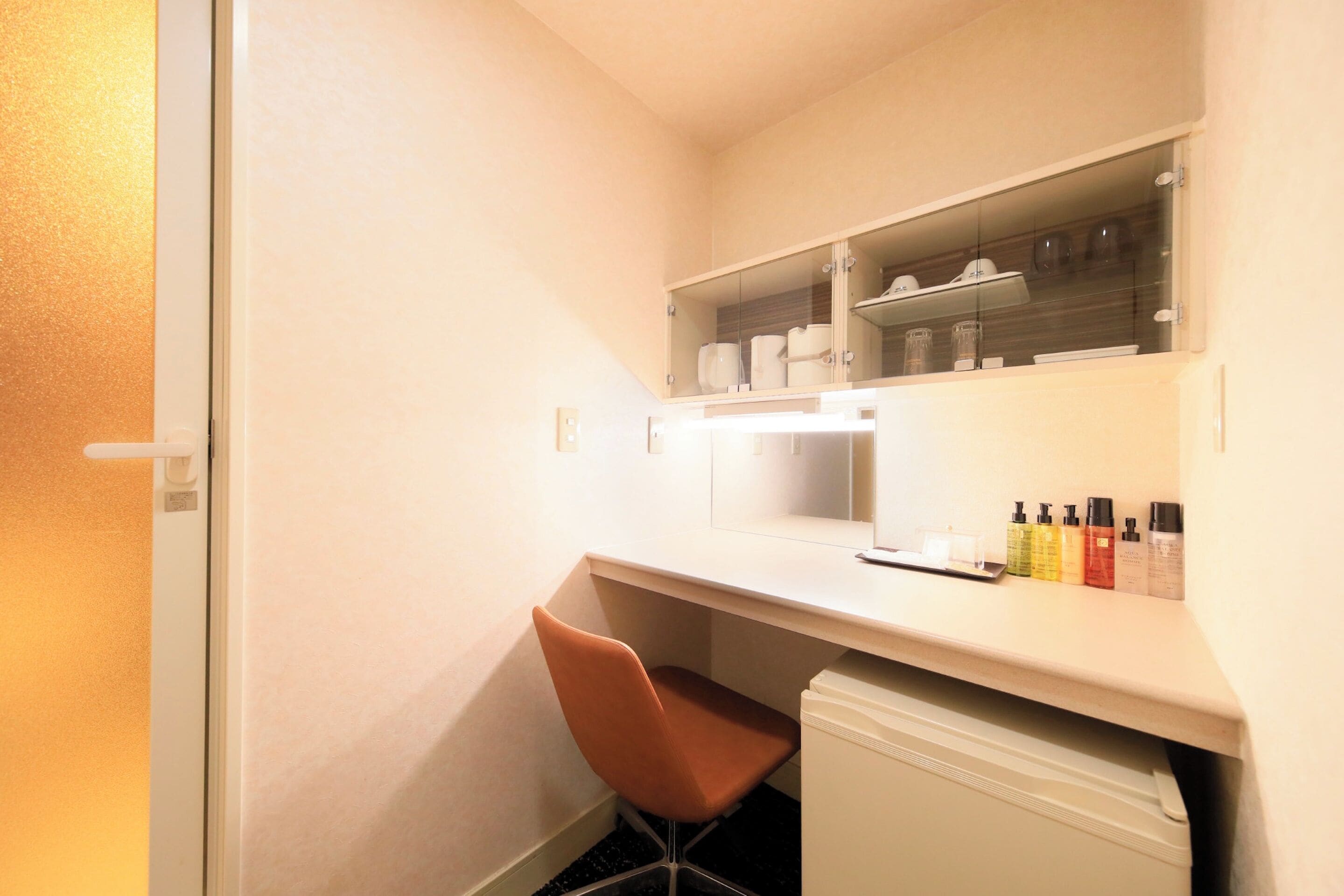 A compact room with a desk, chair, and a small shelf with toiletries.