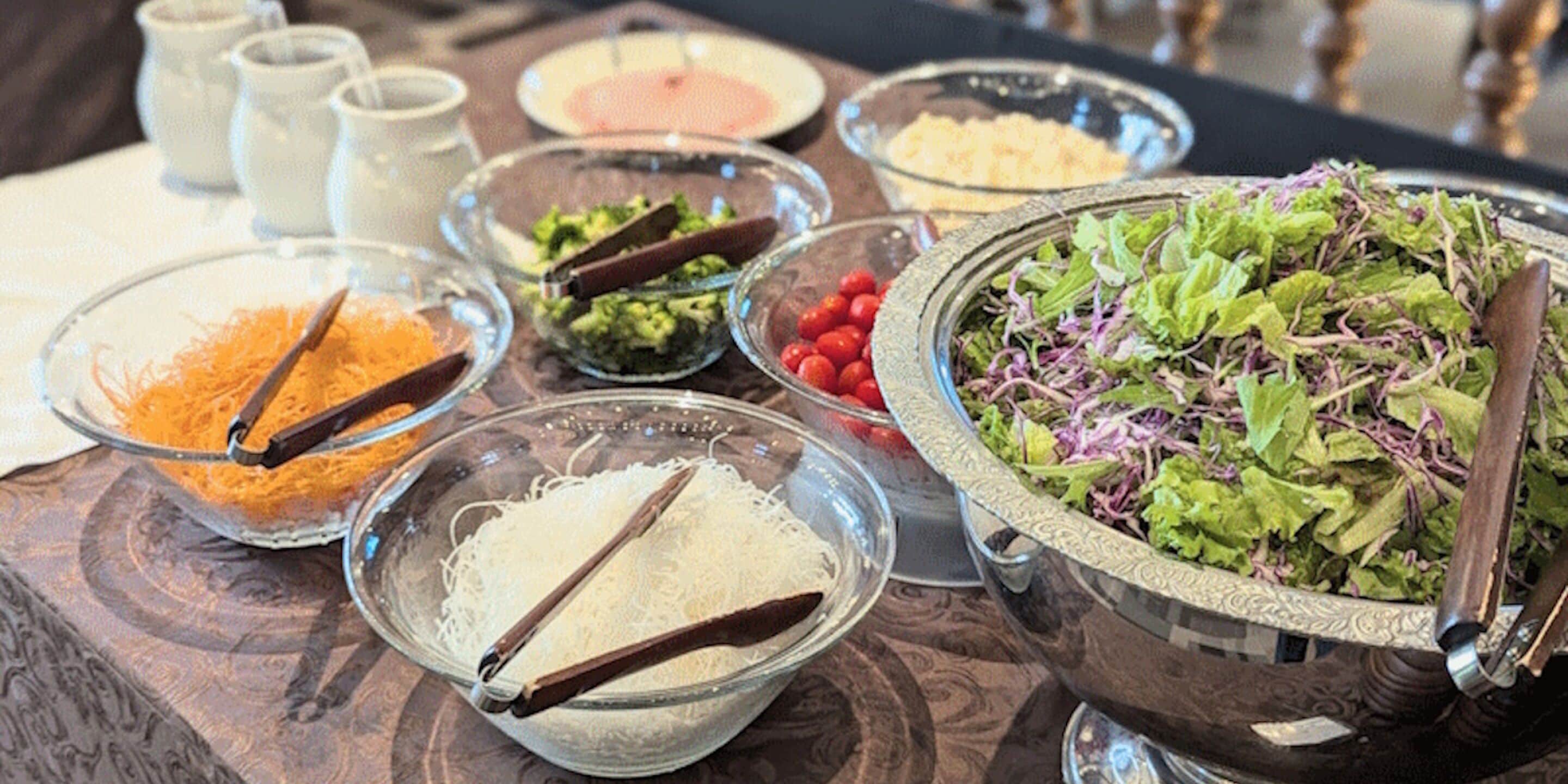 Et bord med forskellige spisemærker, herunder revet ost, en salat og andre ingredienser.