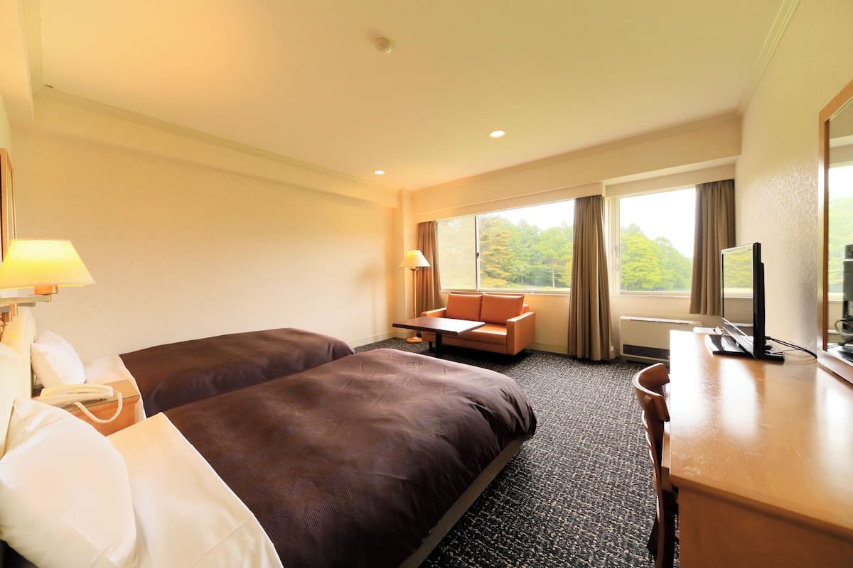 A hotel room with two beds, a desk, a chair, a TV, and a window with curtains.