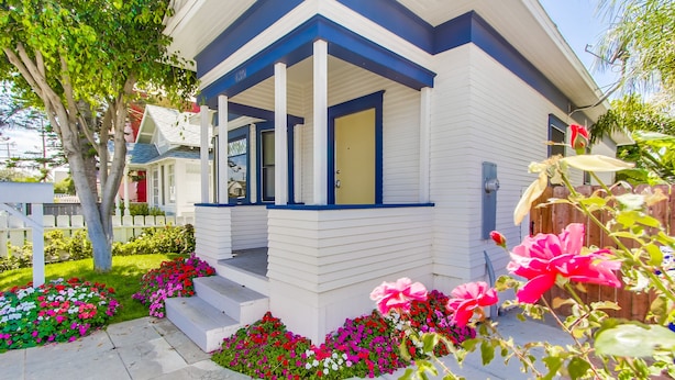Une maison moderne dotée d’un porche abrité, d’une porte d’entrée et d’un jardin bien entretenu, agrémenté de fleurs aux couleurs vives.