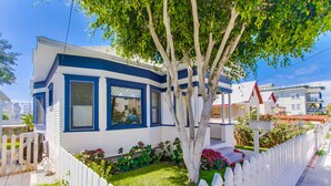 Une maison à deux étages, à l’extérieur bleu et blanc, avec une clôture en bois peinte en blanc et un arbre dans le jardin.