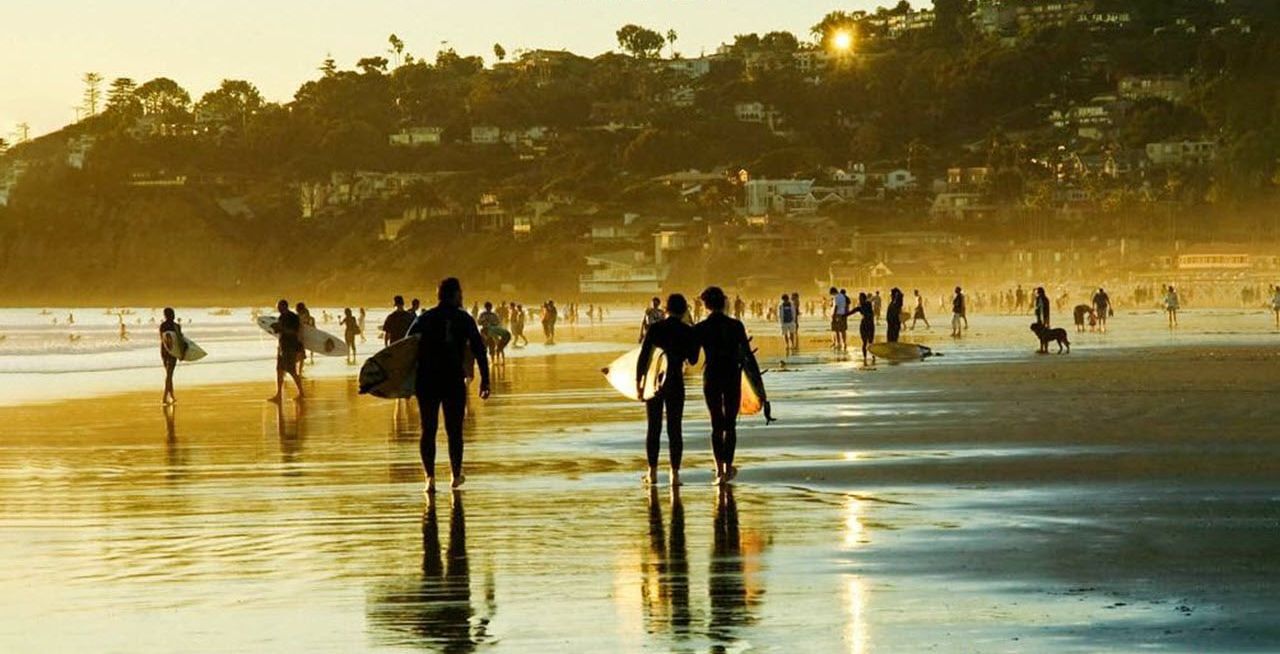 A beach scene with people walking and carrying surfboards, with a logo and text overlay.