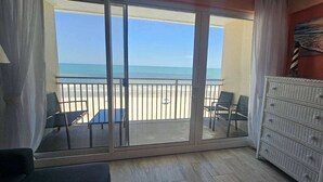 A room with a sliding glass door leading to a balcony with beach views, a small table, two chairs, and a wicker dresser. - Breathtaking DIRECT Ocean Front (Daytona Beach)