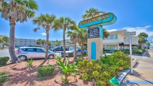 A hotel sign with a tropical theme, palm trees, and a parking lot with cars. - Breathtaking DIRECT Ocean Front (Daytona Beach)