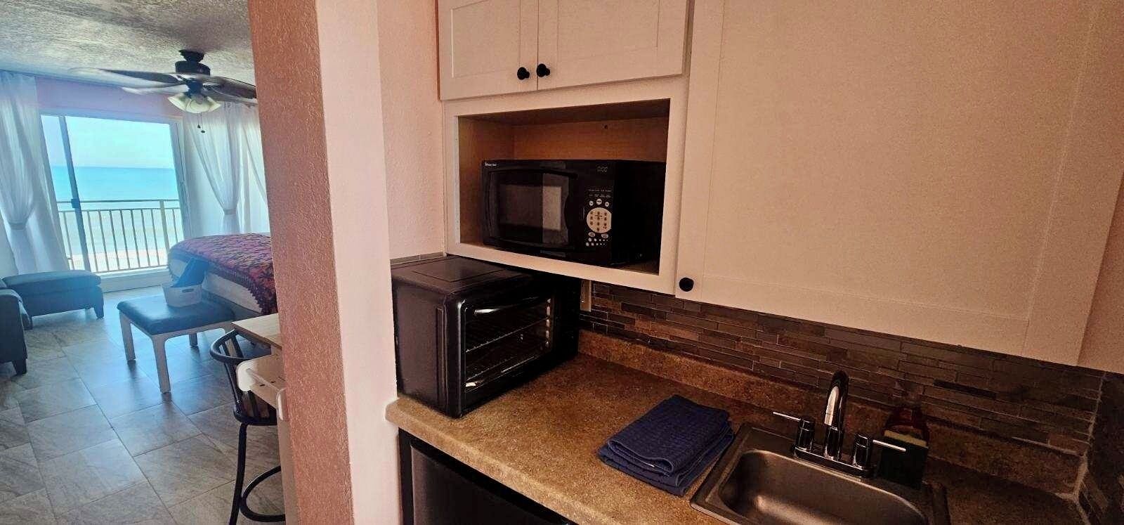 A compact kitchen with a microwave, a toaster, and a sink. There is a balcony with a view of the sea.