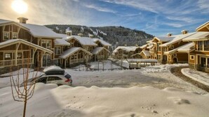 Un refugi cobert de neu amb diversos edificis de fusta, una zona d'aparcament i un paisatge de muntanyes al fons.