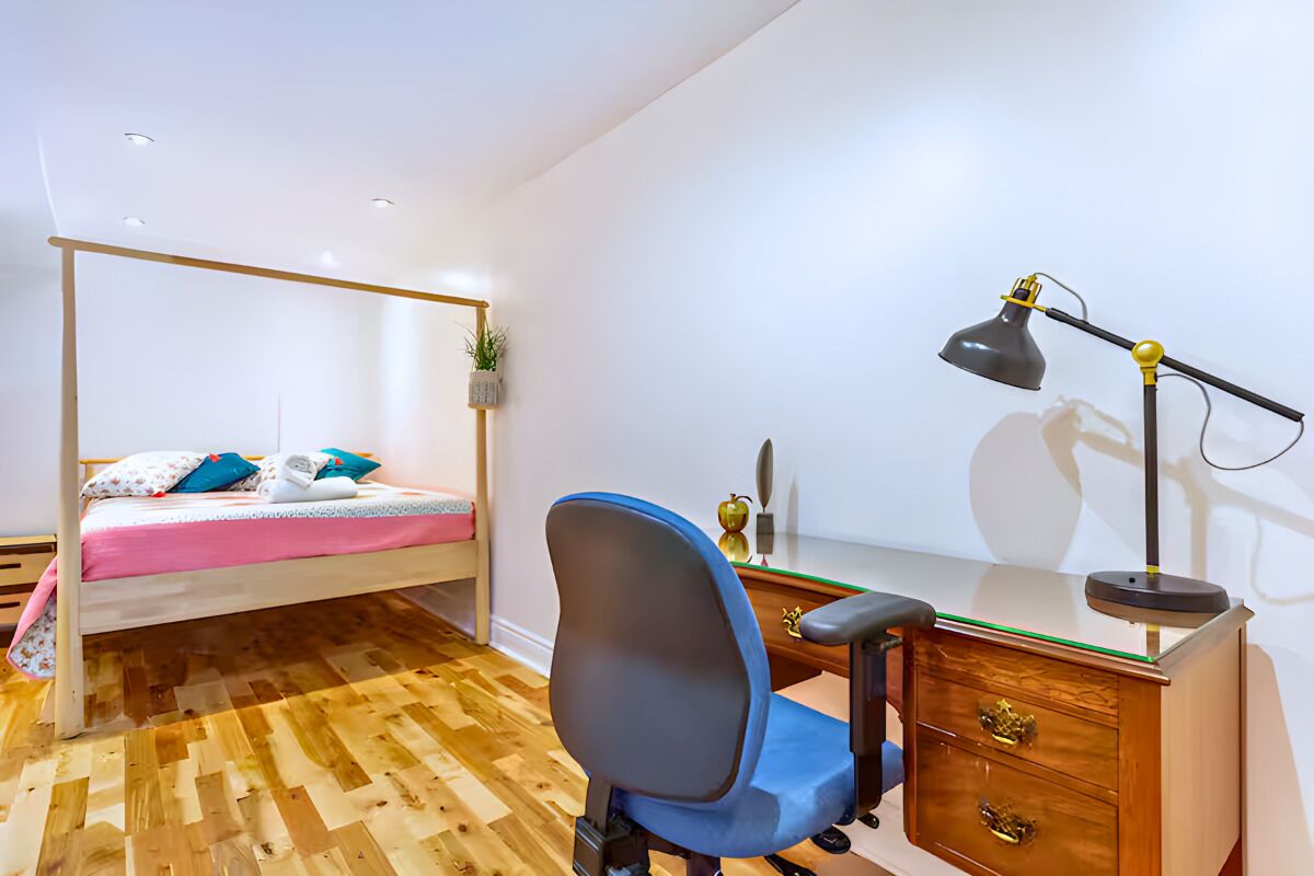 Een slaapkamer met een bed, bureau, stoel en bureaulamp.