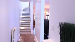 A modern hallway with wooden flooring, white walls, and a staircase leading to another room.