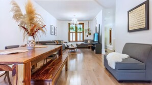 A spacious living room with a wooden dining table, a grey sofa, and a chandelier.