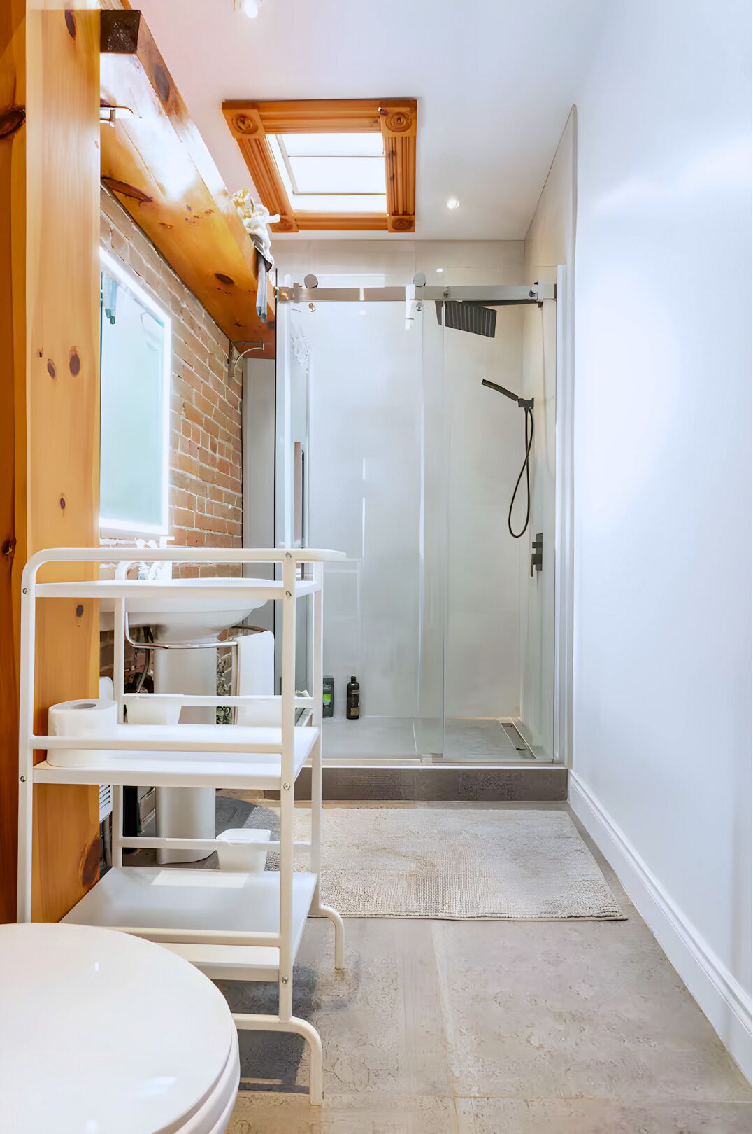 Une salle de bain moderne avec une douche à parois de verre, un lavabo blanc doté d’un meuble de rangement et un plafond en bois.