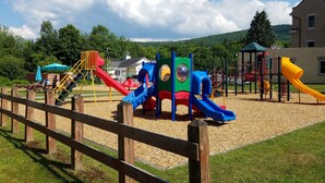A playground with various play structures, a wooden fence, and a building in the background. - whole 🏠! 10% off 7 nts or more, 15% off 28 nts or more (Bethlehem)